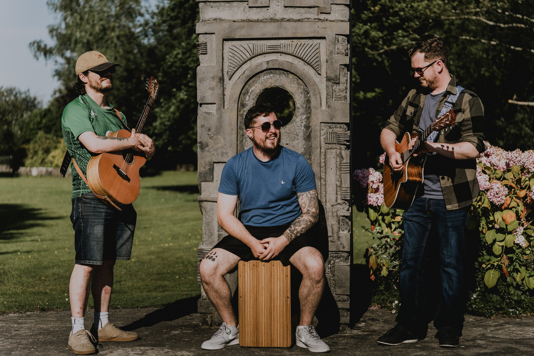 Fir Bolg with guitar, whistle and cajon beside a stone arch